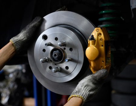 Car mechanic installing two piston brake calipers and disc brake rotor.